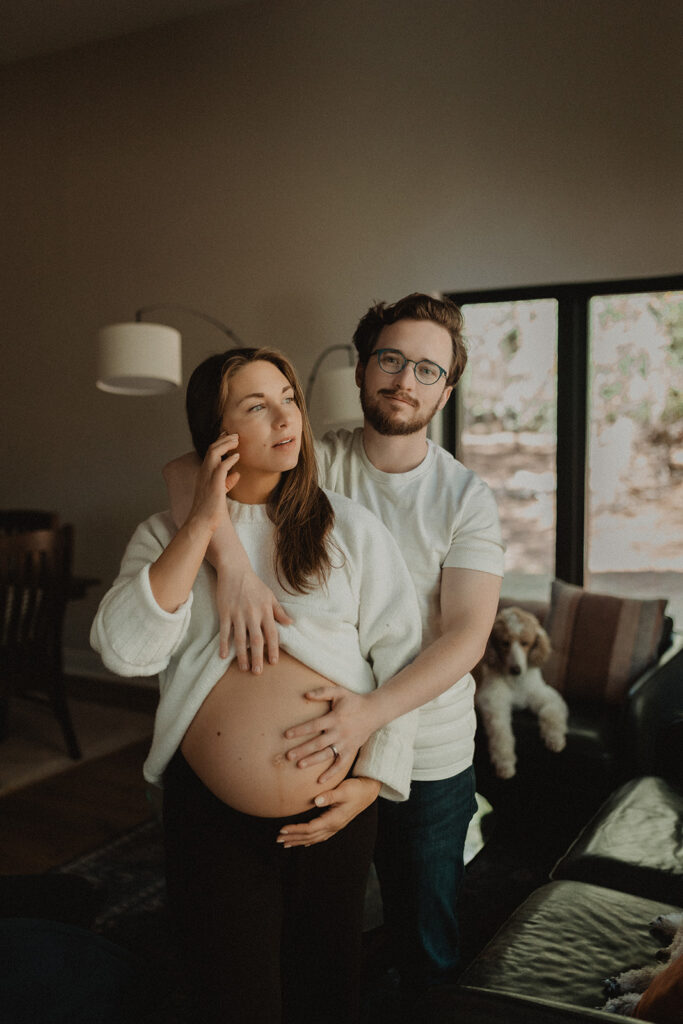 Expecting couple standing together indoors, hands resting on pregnant belly, representing holistic prenatal support and care inspired by Moonshadow Medical Massage.