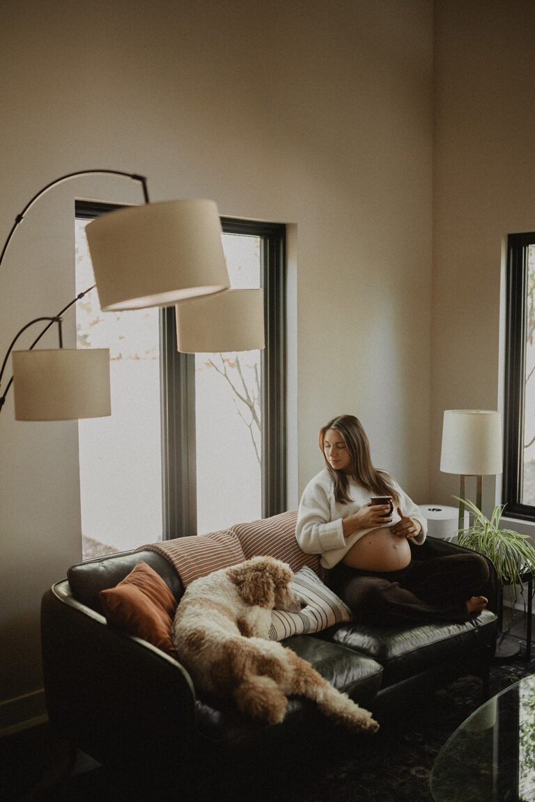 Cozy lifestyle maternity photo of a pregnant woman resting on a sofa with her dog, reflecting stress relief and nurturing prenatal massage experiences at Moonshadow Medical Massage.