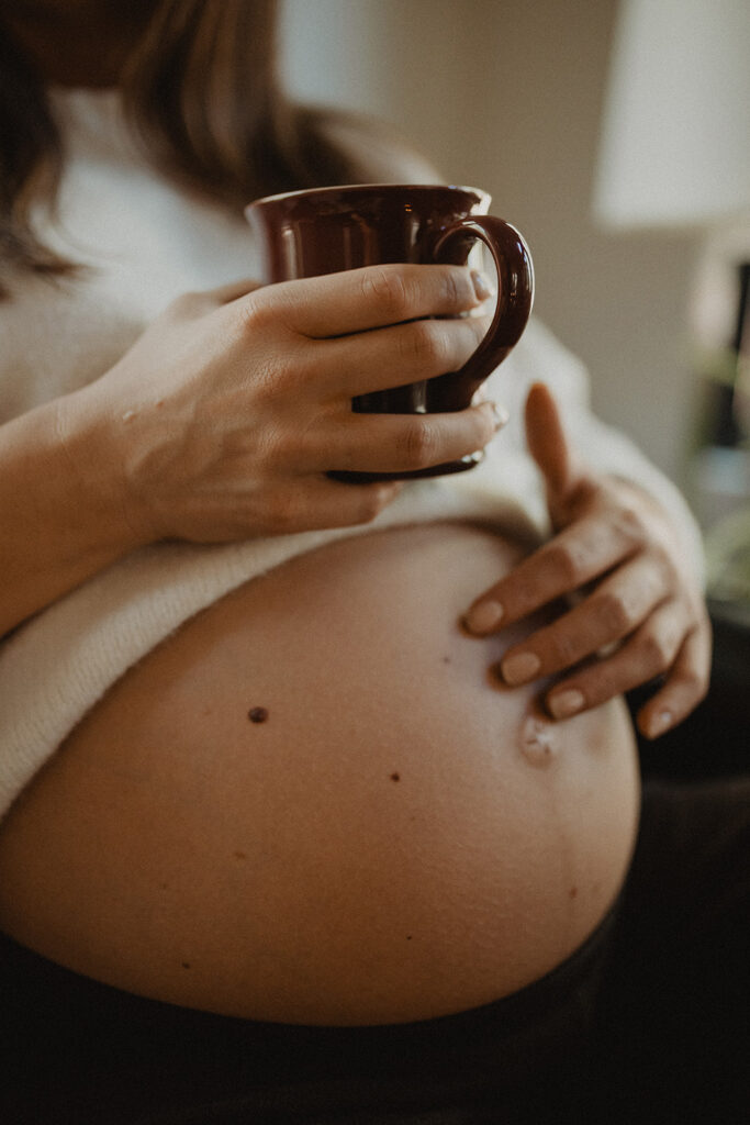 Close-up maternity detail of pregnant belly and hands holding a warm mug, emphasizing relaxation, circulation, and comfort promoted by Moonshadow Medical Massage prenatal services.