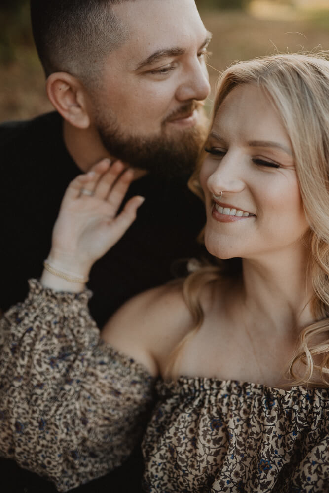 Close-up maternity portrait of a smiling pregnant woman with long blonde hair leaning toward her partner during an outdoor session. Captured by Victoria Vasilyeva Photography