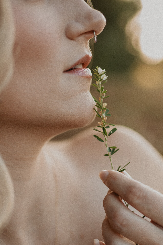Artistic close-up of a woman holding a small sprig of greenery near her lips during a soft, golden-hour maternity session. Photo by Victoria Vasilyeva Photography outdoor near Natural Beginnings Birth Center.