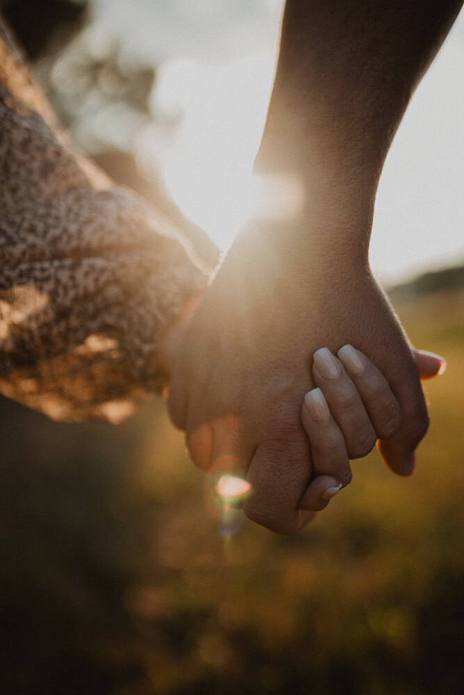 Close-up of an expecting couple holding hands in warm sunset light during an outdoor maternity session with Raleigh maternity photographer - Victoria Vasilyeva Photography.