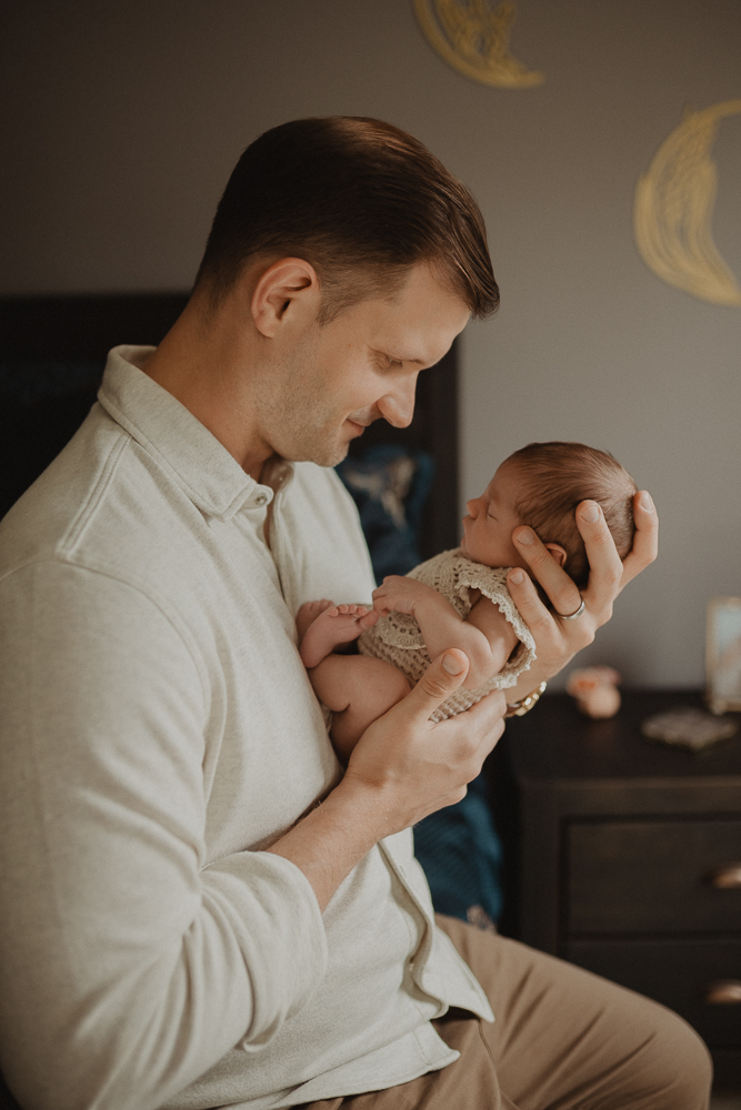 Father in light shirt cradling his baby girl while standing in the nursery, demonstrating hands-on support for postpartum and feeding care. Newborn session by Victoria Vasilyeva Photography.
