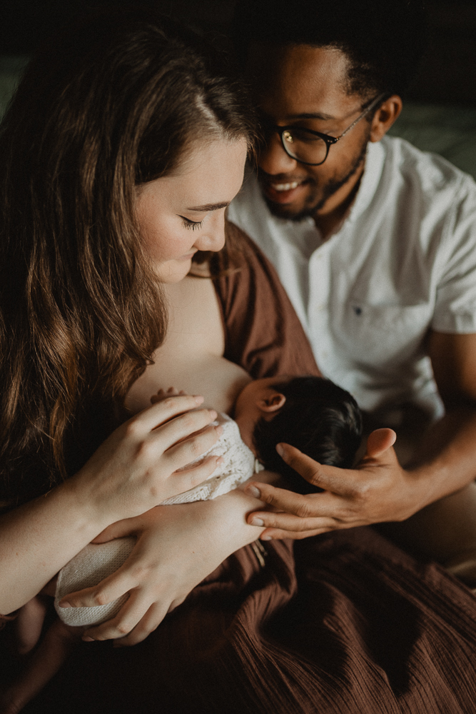 New parents smiling while supporting the mother during breastfeeding, emphasizing connection and guidance in early lactation.