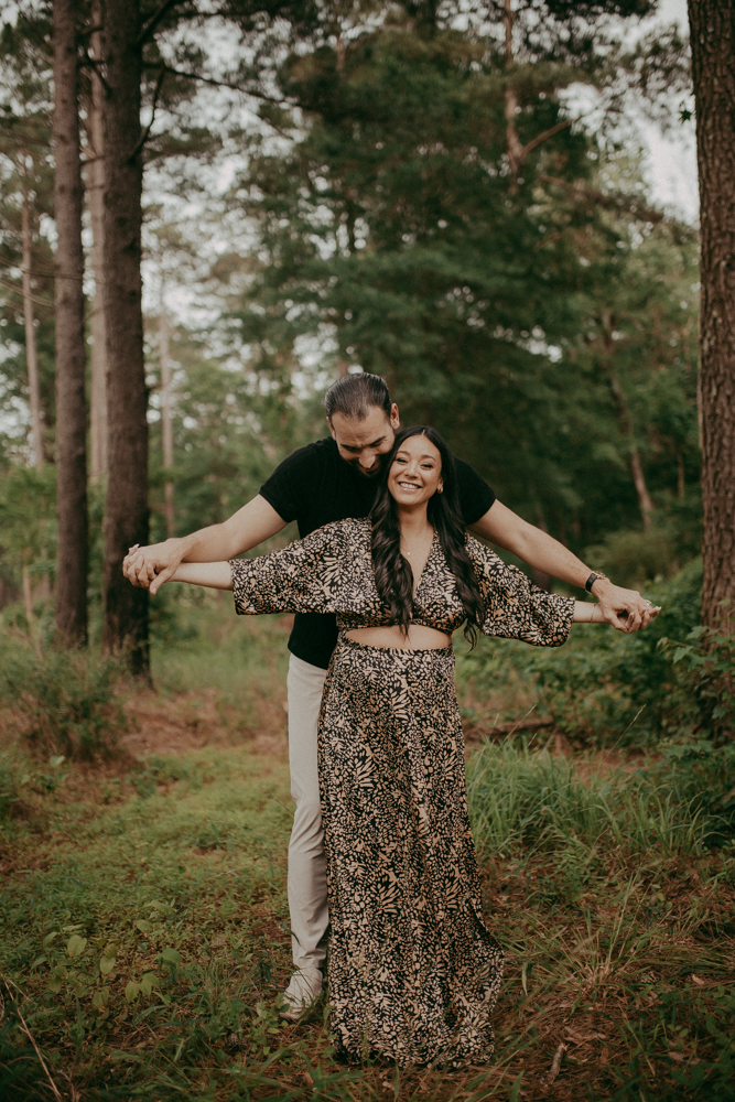Playful maternity photo of an expecting couple holding hands and smiling in a natural outdoor setting. Maternity portrait session in Cary, NC by Victoria Vasilyeva Photography.