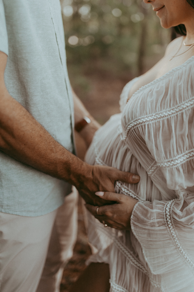 Intimate maternity detail showing parents’ hands resting gently on a baby bump, symbolizing love and support.