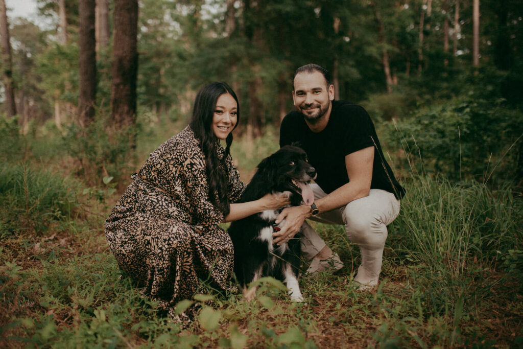 Expecting parents sitting together in a forest with their dog, sharing a joyful moment during a maternity session. Maternity portrait session in Cary, NC by Victoria Vasilyeva Photography.