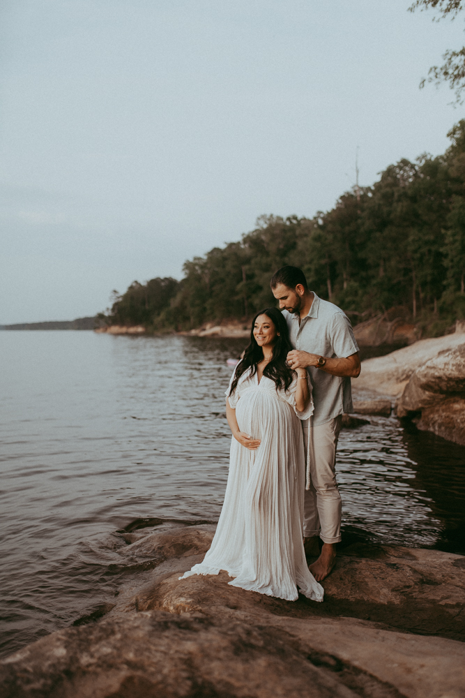 Wide maternity portrait of a couple standing barefoot by the water at sunset, capturing a calm and emotional moment, maternity photography Cary NC by Victoria Vasilyeva Photography.