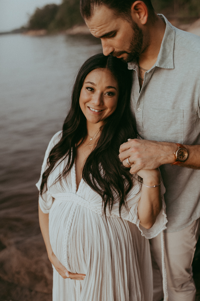 Close-up maternity portrait of a smiling expecting mother with long black hair with her partner gently resting his head near hers, maternity photography Cary NC by Victoria Vasilyeva Photography.