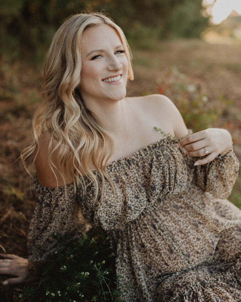 Pregnant woman with blonde hair sitting in golden sunset light in a flowy patterned dress. Maternity portrait by Victoria Vasilyeva Photography for a blog about Natural Beginnings Birth Center.