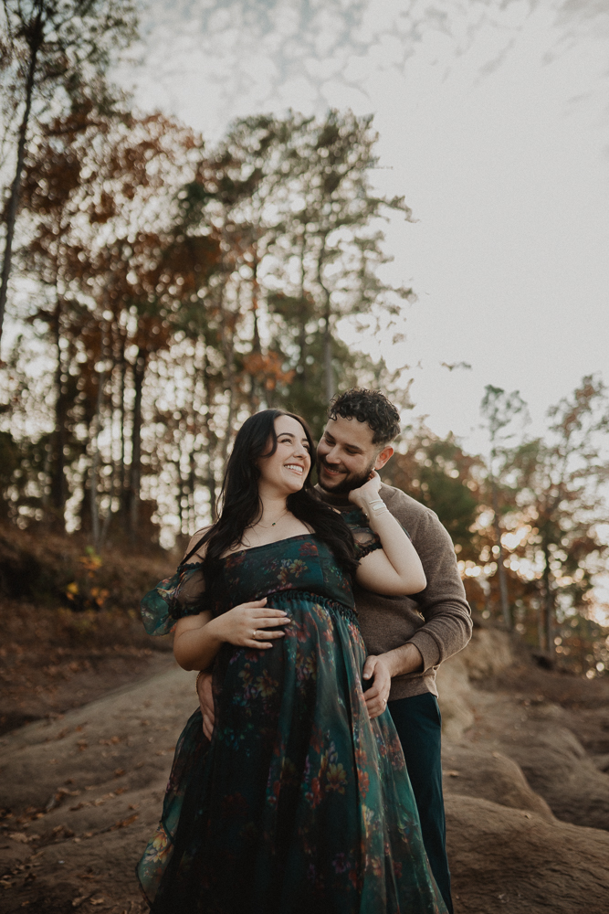 Expecting parents standing together on a rock in a wooded area during a maternity photo session in Greensboro, North Carolina. Greensboro maternity photographer.