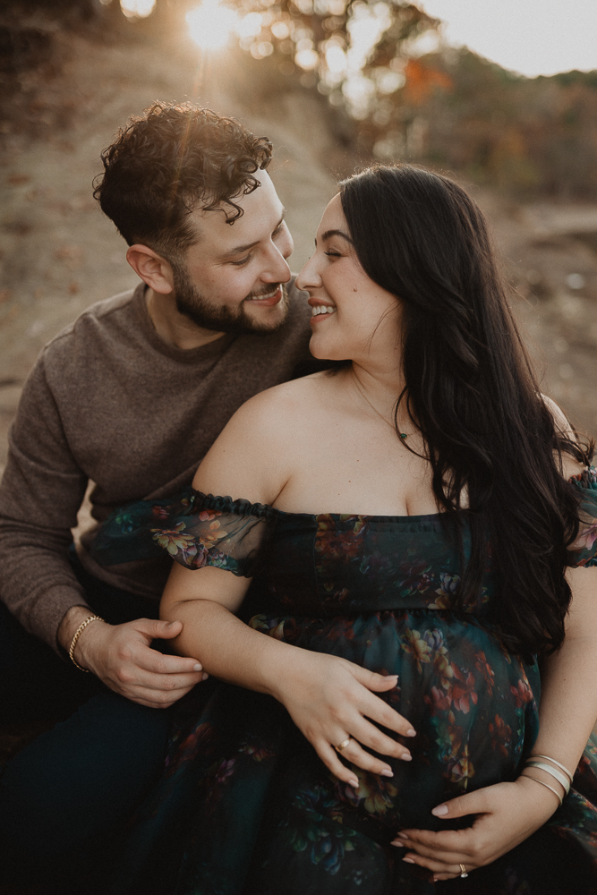 Pregnant woman sitting with her partner on rocks during an intimate outdoor maternity photo session in Greensboro, NC. Romantic maternity photography by Victoria Vasilyeva Photography.