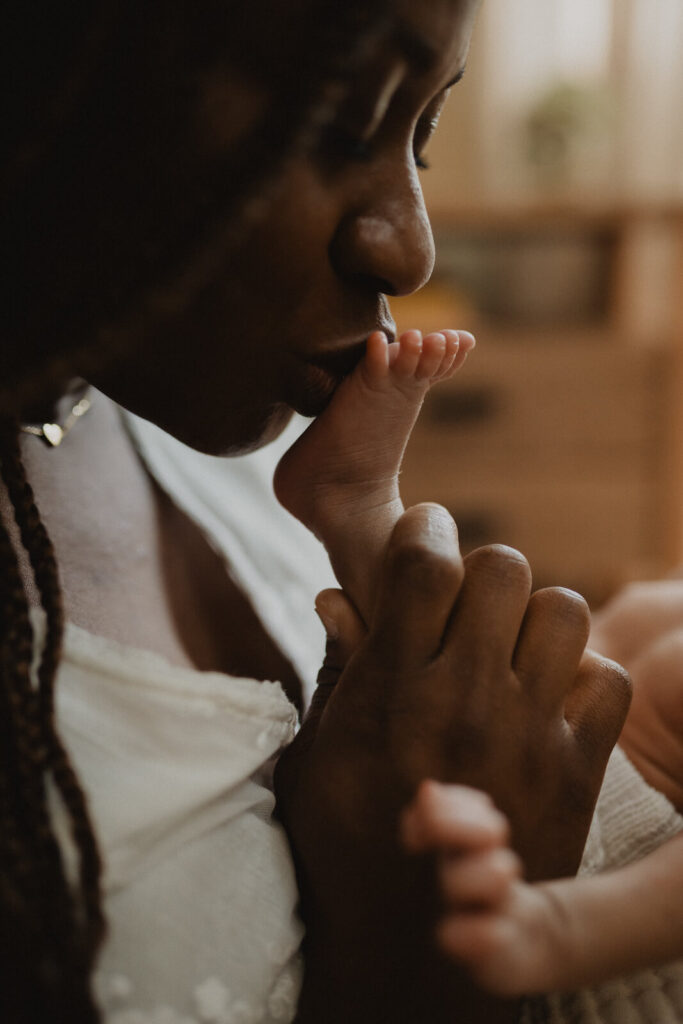 A mother gently kisses her newborn's tiny foot during an intimate in-home newborn session photographed by Raleigh newborn photographer - Victoria Vasilyeva Photography.