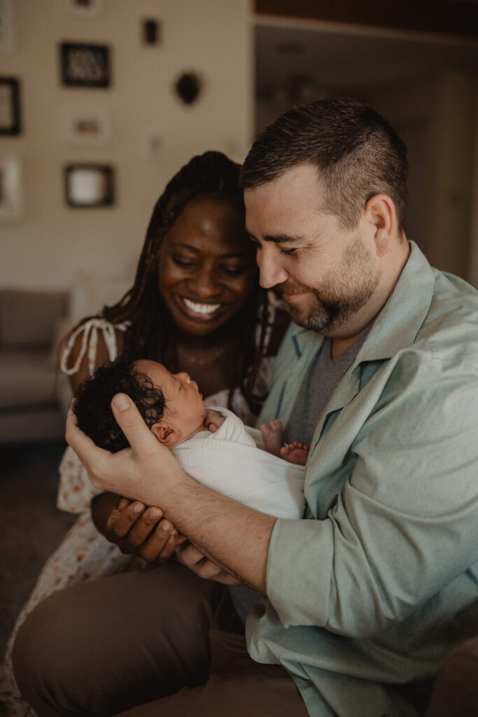Goodnight Sweet Baby. Smiling parents admire their newborn baby boy in their arms during a heartfelt in-home newborn session captured by Raleigh newborn photographer - Victoria Vasilyeva Photography.