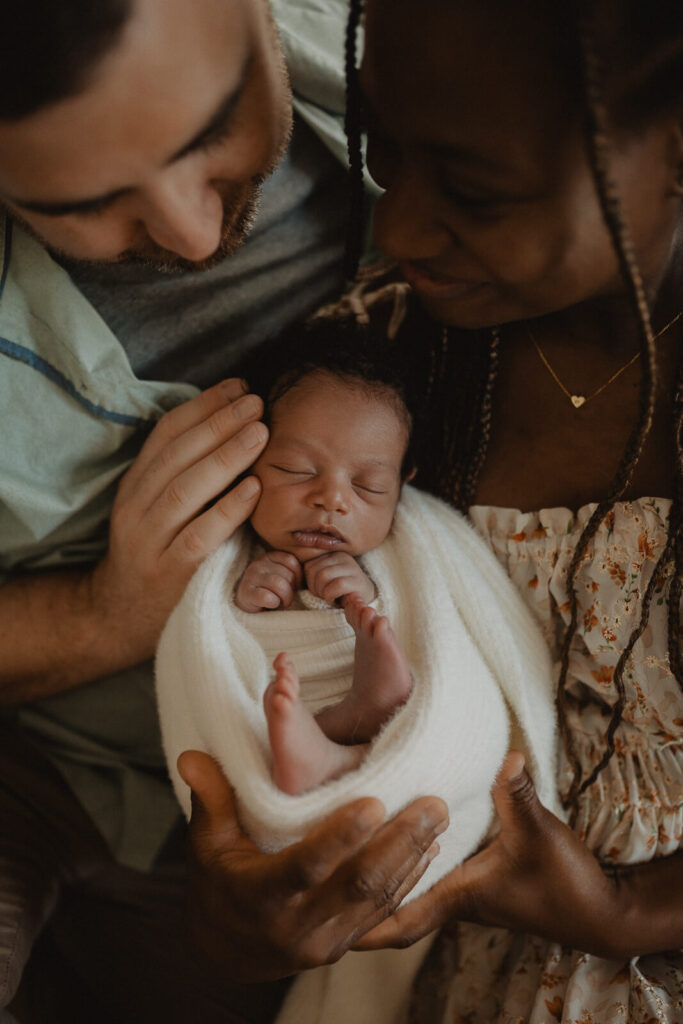 A peacefully sleeping newborn is cradled in the loving hands of both parents during a lifestyle session photographed by Raleigh newborn photographer - Victoria Vasilyeva Photography, preserving the fleeting beauty of the first weeks at home.
