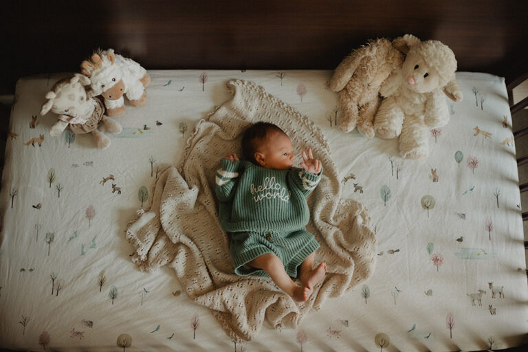 Newborn baby girl lying in a crib wearing a green outfit during a cozy in-home newborn photography session in Raleigh, NC by Victoria Vasilyeva Photography.