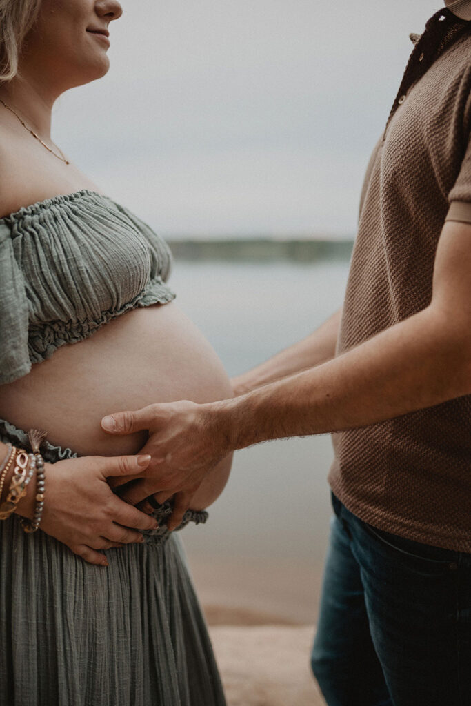Close-up of an expecting couple holding their baby bump during a lakeside maternity session by a Wake Forest photographer.