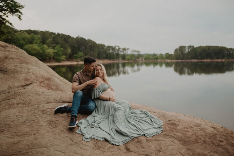 Romantic maternity portrait on rocky shoreline overlooking the lake, captured by a Wake Forest photographer.
