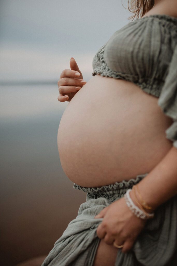 Artistic close-up of a baby bump during a lakeside maternity photoshoot by a Wake Forest photographer.