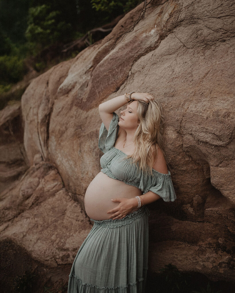 Outdoor maternity portrait of an expectant mother leaning against natural rock formations, photographed by a Wake Forest photographer.