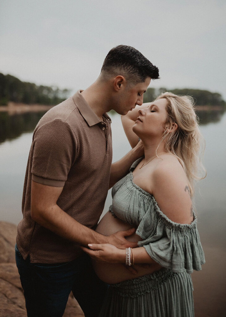 Intimate maternity portrait of an expecting couple sharing a quiet moment by the water with a Wake Forest photographer.