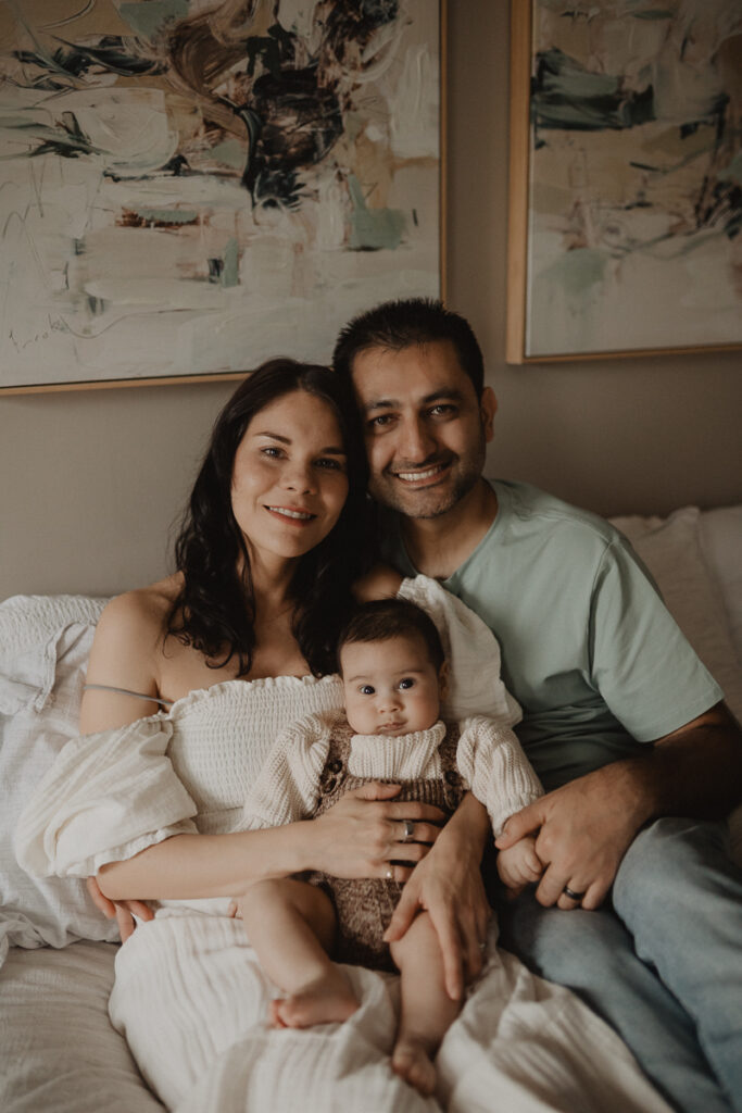 Chapel Hill family photographer photographing a family portrait of parents and their baby boy sitting together on a bed at home.