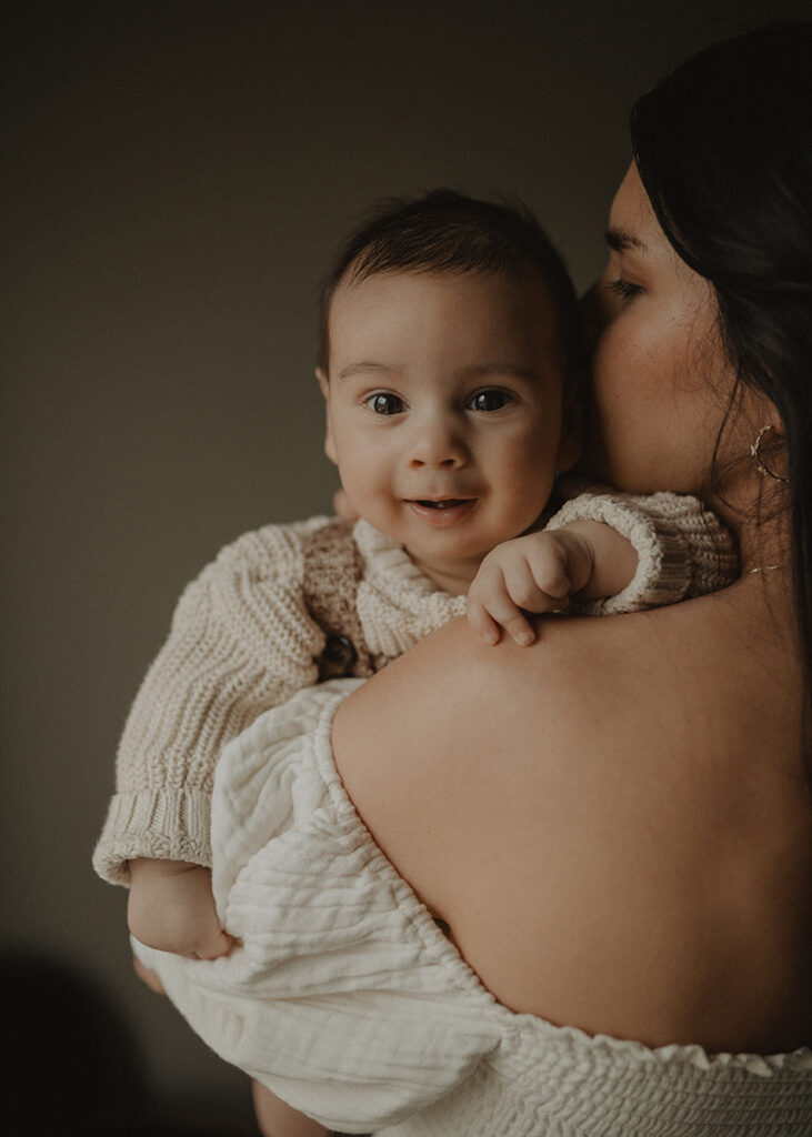Smiling baby boy looking into the camera while being held by his mother during a natural light family session in Chapel Hill, North Carolina.