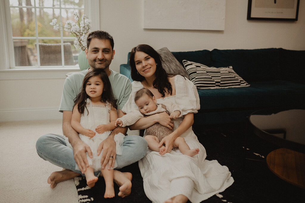 Family of four sitting in the living room during an in-home Chapel Hill family photo session, welcoming their newest addition.