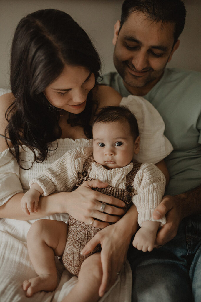 In-home family photography in Chapel Hill featuring parents cuddling their baby boy, capturing genuine connection and natural light.