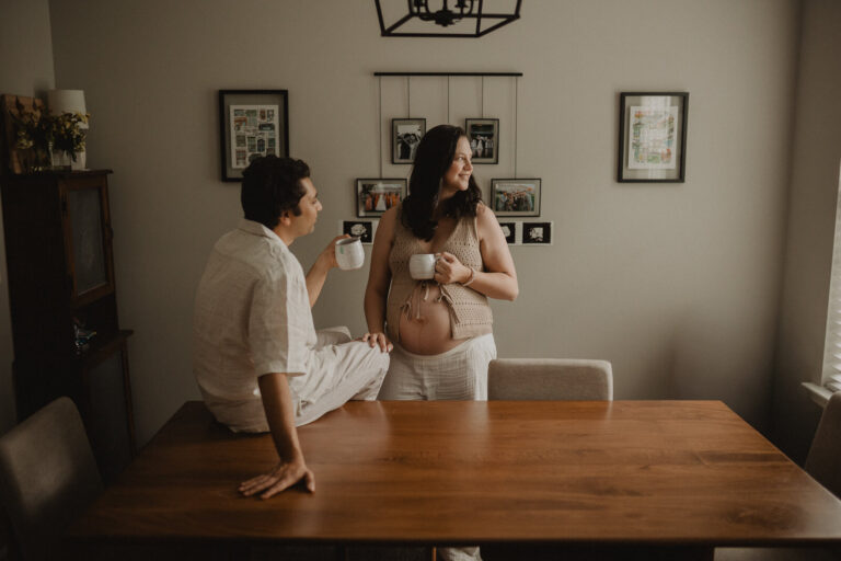 Parents-to-be enjoying a quiet morning together with coffee mugs in hand, captured in their home during a natural and candid maternity photo session in Holly Springs.