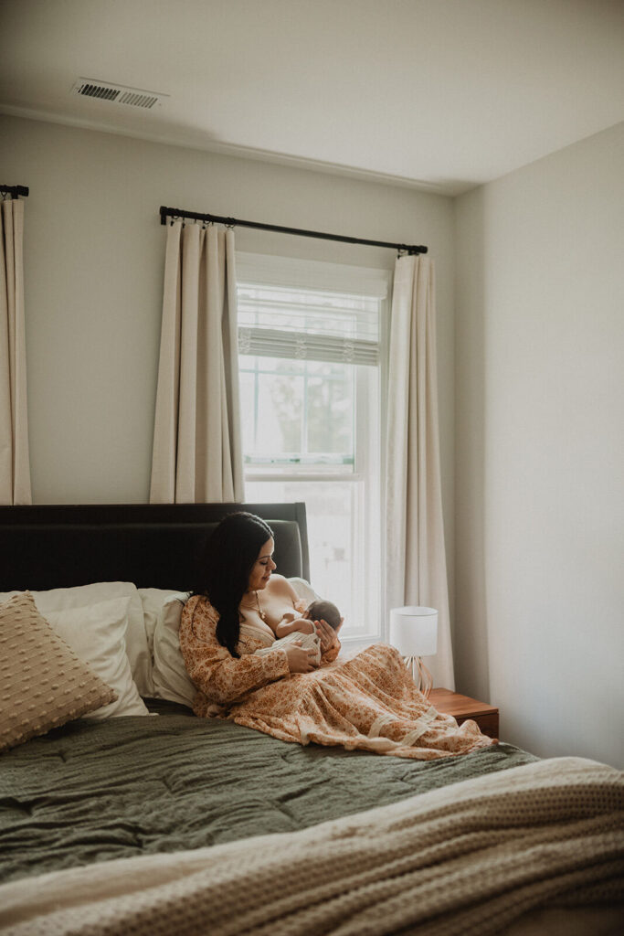 Mother breastfeeding her newborn baby boy on a bed in a bright bedroom during a cozy lifestyle newborn session, reflecting guidance from Honeysuckle Lactation consultant.