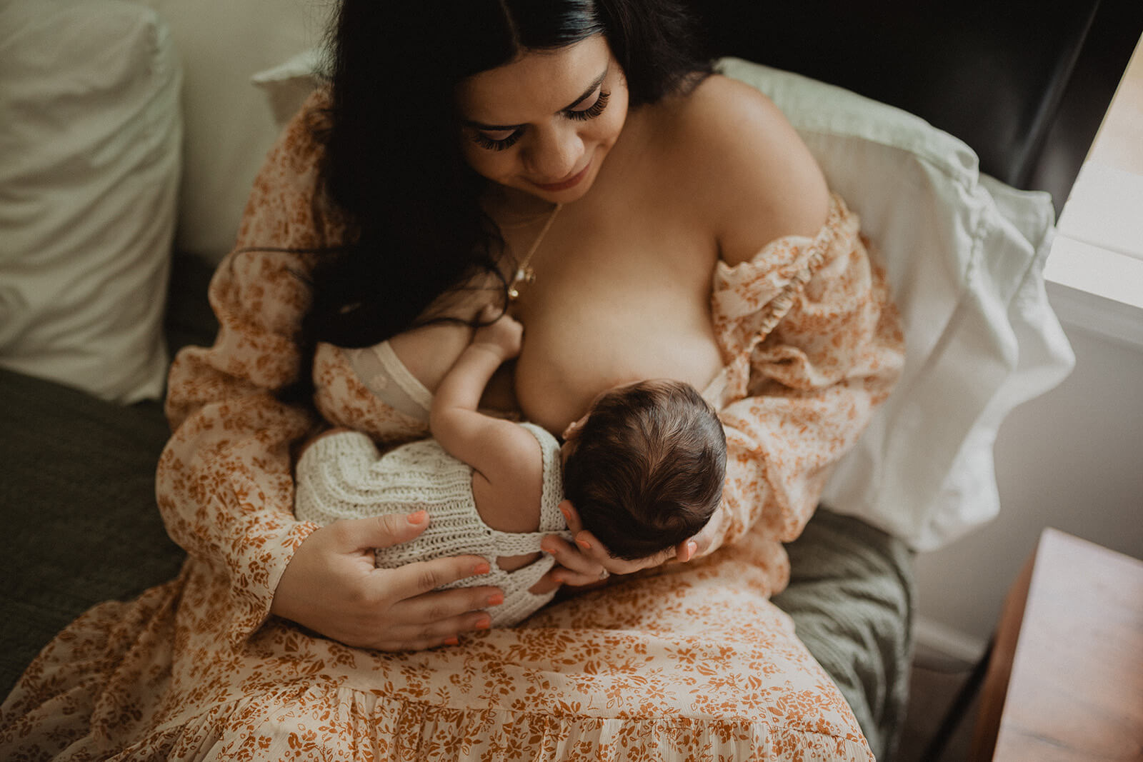 Mother breastfeeding her newborn baby boy in a cozy bedroom during a lifestyle newborn photography session in Raleigh, NC.