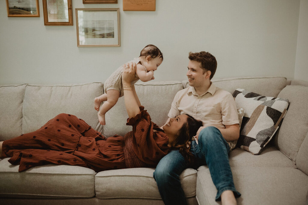 Mother lifting her smiling baby boy above the sofa.