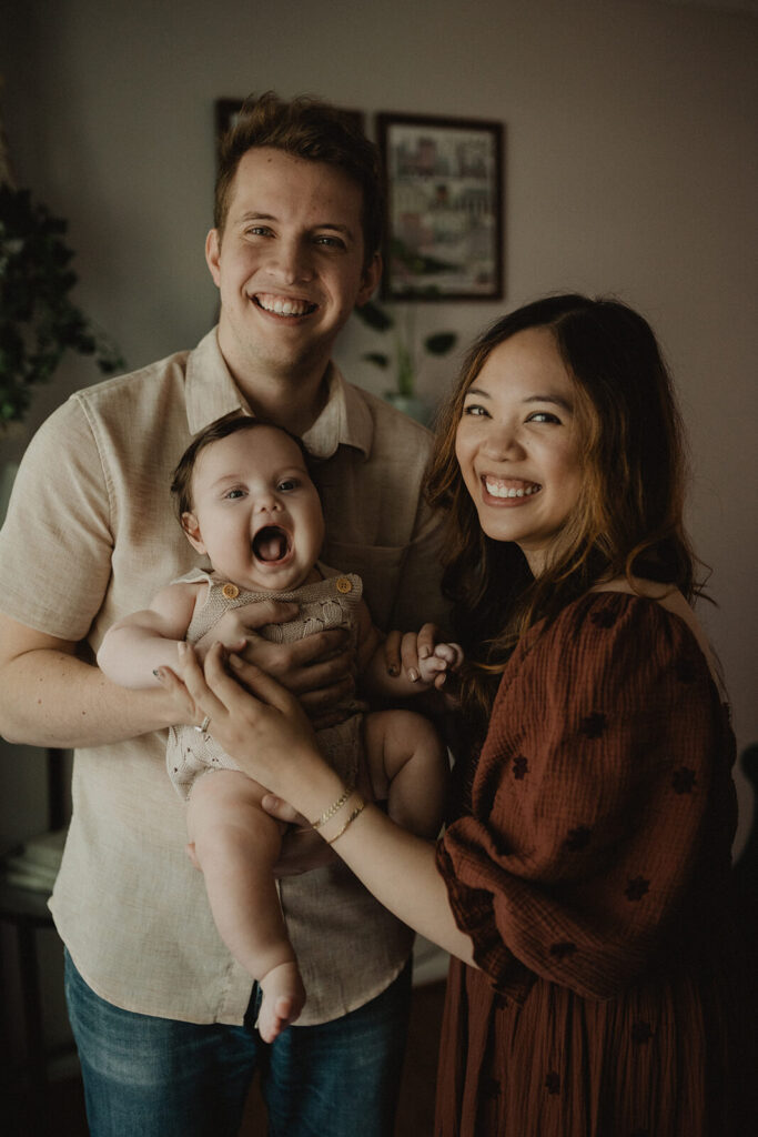 Happy family portrait during an in-home lifestyle session with smiling parents and baby boy, photographed by Victoria Vasilyeva Photography for a Raleigh sleep coach feature.