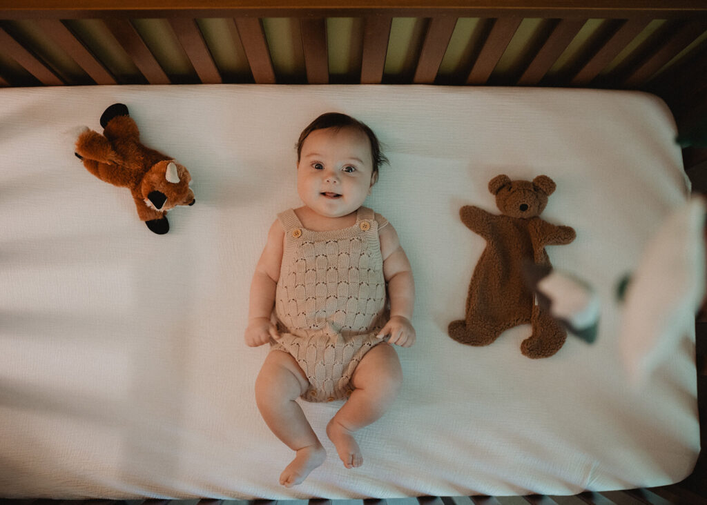 5 months old baby boy lying in a crib beside plush woodland toys during a lifestyle family session, illustrating a peaceful sleep environment recommended by a Raleigh sleep coach.