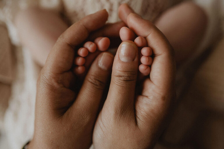 Close-up of a newborn's tiny feet being gently held by loving parents, symbolizing the support and reassurance families often find through a virtual sleep consultant.