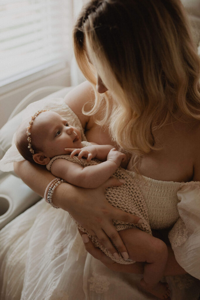 Natural lifestyle portrait of a mother holding her baby girl by the window, photographed by Victoria Vasilyeva Photography in Raleigh NC.
