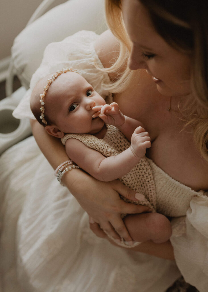 Baby girl looking toward the camera while being held by her mother during a newborn session with Victoria Vasilyeva Photography in Raleigh NC.
