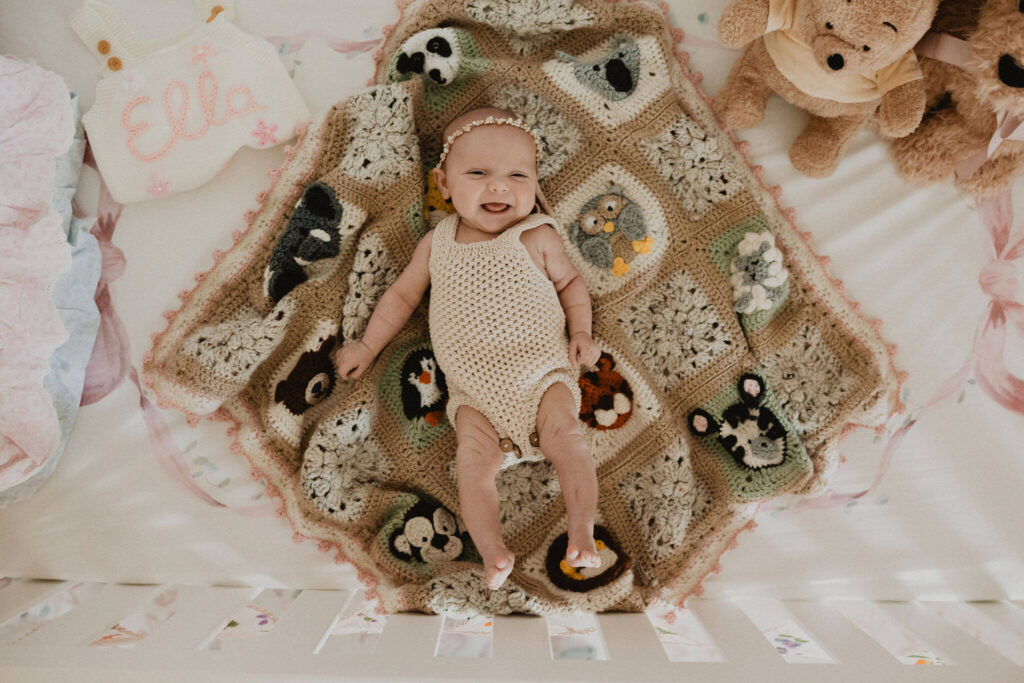 Smiling baby girl on a handmade by grandmother crochet blanket photographed by Raleigh NC newborn photographer Victoria Vasilyeva Photography.