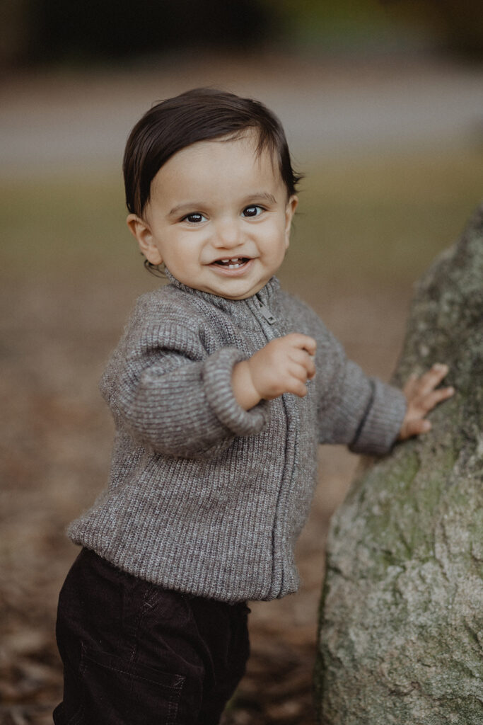 Smiling toddler boy outdoors during a fall family photo session at a pumpkin patch near Raleigh, NC, by Victoria Vasilyeva Photography.