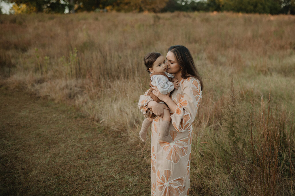 Mother kissing her baby during a natural fall family photo session at a pumpkin patch near Raleigh, North Carolina. Photo session took place at Crossroads Corn Maze in Wendell, NC.
