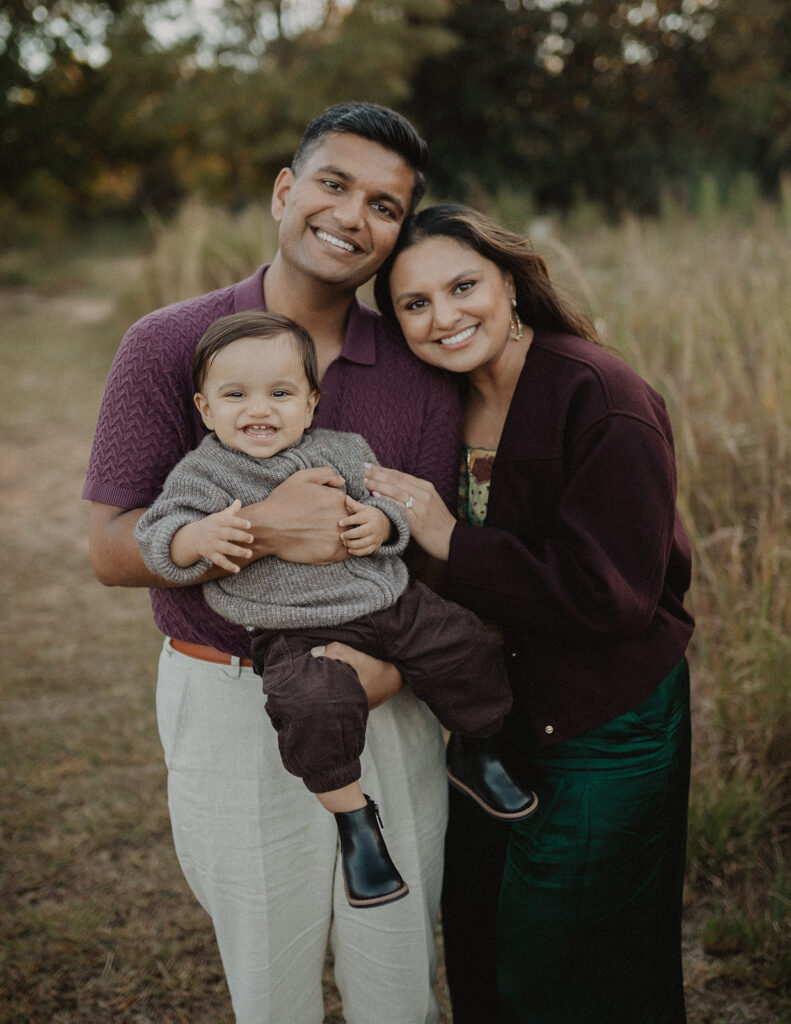 Happy family of 3 with their smiling baby boy during a fall pumpkin patch family photography session in Raleigh, North Carolina.