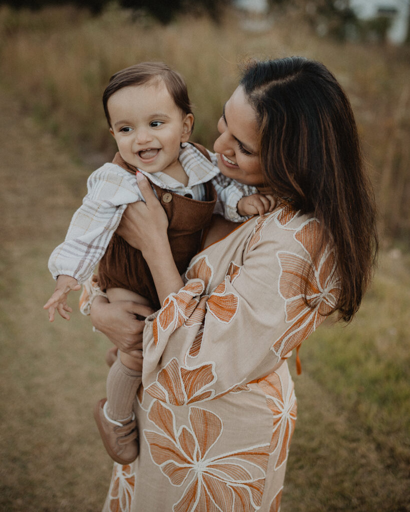 Mother holding her smiling baby boy at Grasshopper Farms in Knightdale, NC during a warm pumpkin patch family photography session.