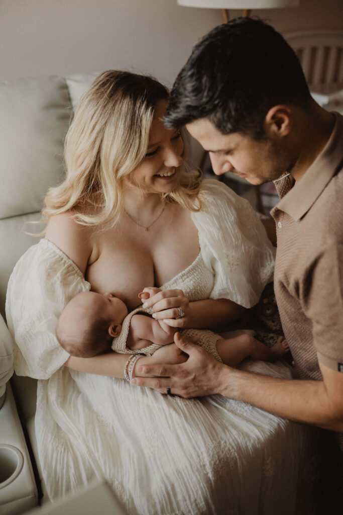 Mother breastfeeding her newborn while father looks lovingly at their baby during a lifestyle family newborn session by Victoria Vasilyeva Photography, Raleigh NC newborn photographer.