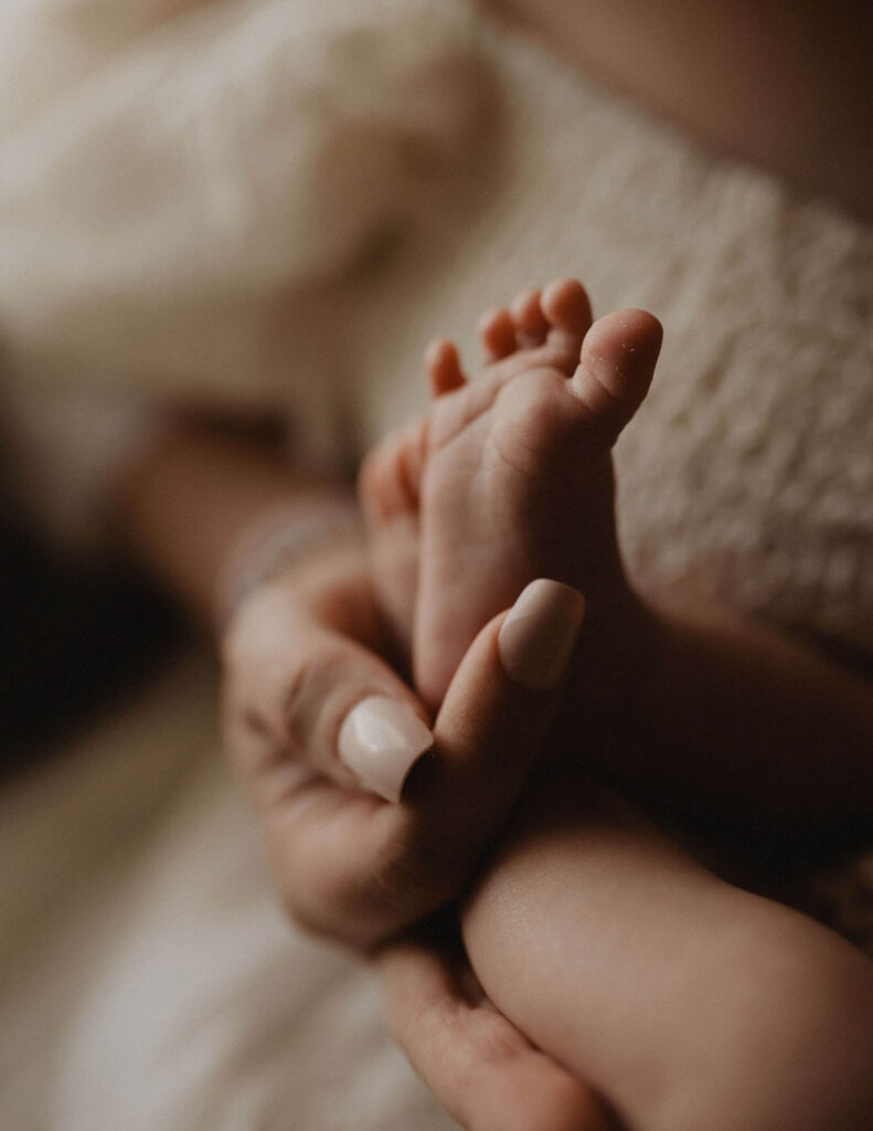 Close-up detail of tiny newborn baby feet held gently in a mother's hand, photographed by Victoria Vasilyeva Photography during an in-home newborn session in Raleigh NC.