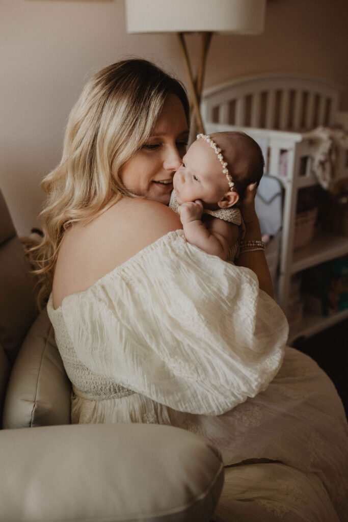 Mother cuddling her newborn baby girl in a softly lit nursery during a natural lifestyle newborn session by Victoria Vasilyeva Photography in Raleigh NC.