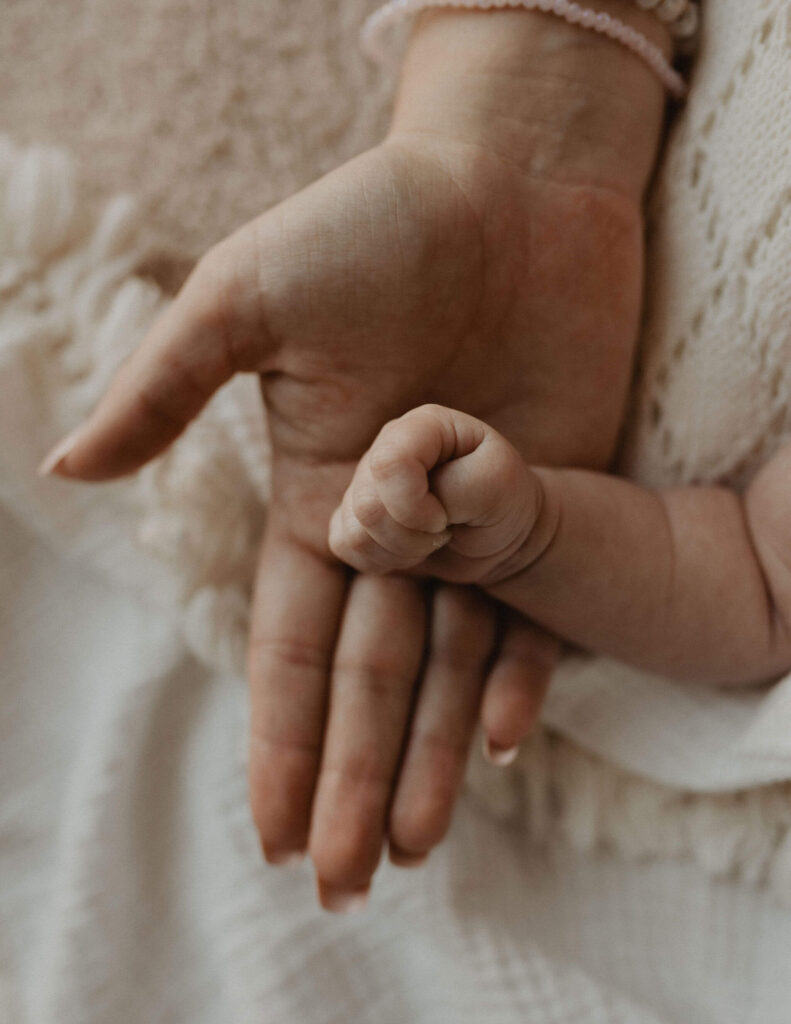Close-up of a newborn baby's tiny hand resting in her mother's hand during an intimate Raleigh newborn photography session by Victoria Vasilyeva Photography.