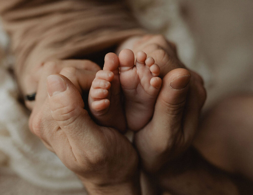 Close-up of tiny newborn baby feet cradled in a parent's hands during an in-home newborn photography session by Victoria Vasilyeva Photography, Raleigh NC newborn photographer.
