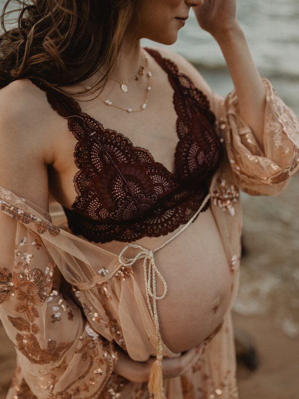 Close-up of a mother-to-be with dark hair wearing a lace robe and holding her belly. Victoria Vasilyeva Photography. Raleigh NC maternity photography.