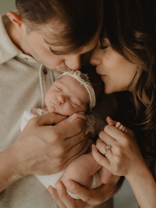 New parents gently holding their newborn baby girl during an in-home newborn photo session in Raleigh, NC. Lifestyle newborn photography by Victoria Vasilyeva Photography.